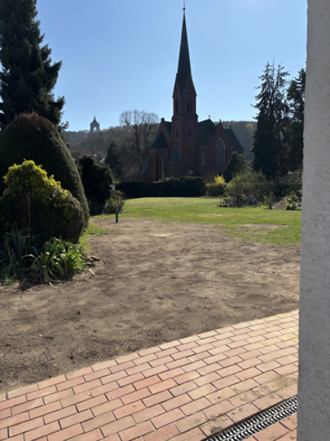 Karimli Haus & Garten Service- Blick von einem Garten auf eine Kirche mit markantem Turm